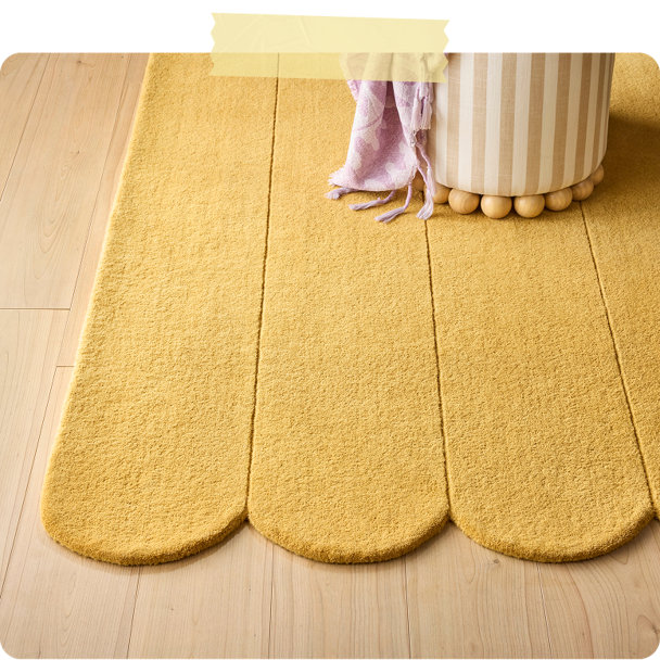 Yellow scalloped-edge area rug on light wood floor with striped ottoman