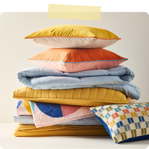 Colorful bedding stack including pillows, comforters, and quilts in yellow, cora