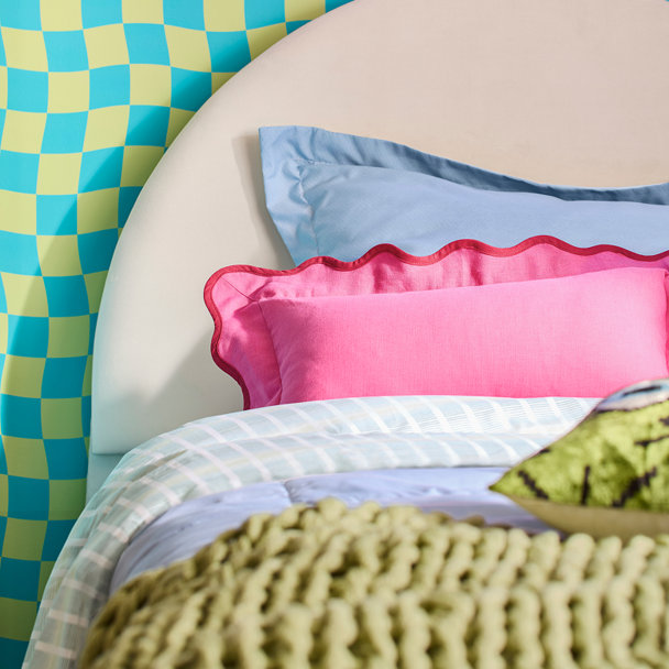 Close-up of a modern bed featuring a rounded cream headboard, light blue bedding