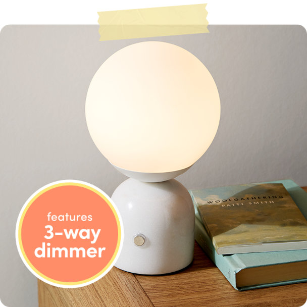 White globe table lamp with rounded ceramic base on a wooden desk beside stacked